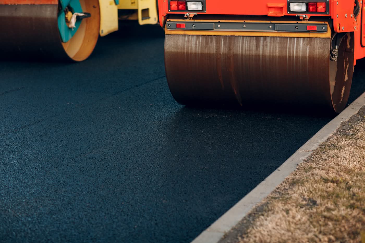 Road roller compacting fresh asphalt near curb