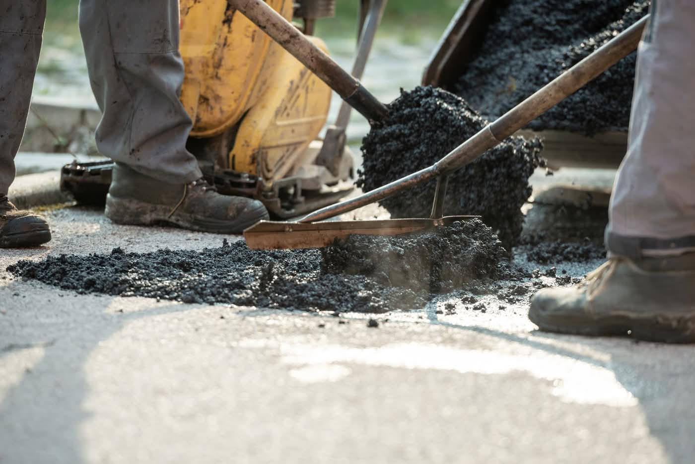 Workers repairing asphalt road with shovels and hot mix