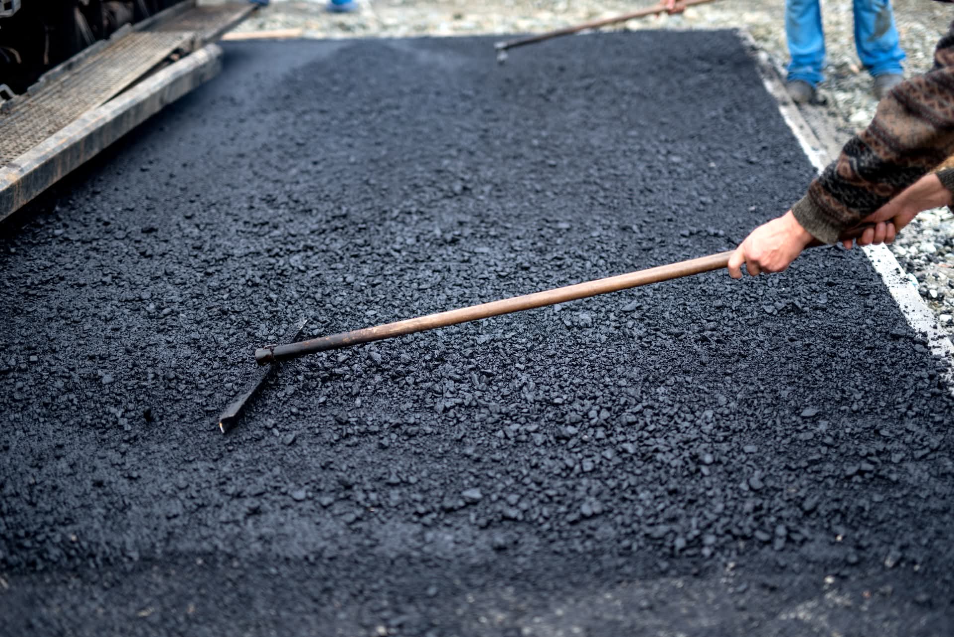 Worker spreading fresh asphalt with rake on road