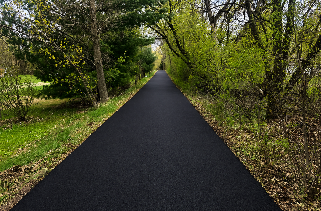 Freshly paved asphalt path through green wooded park