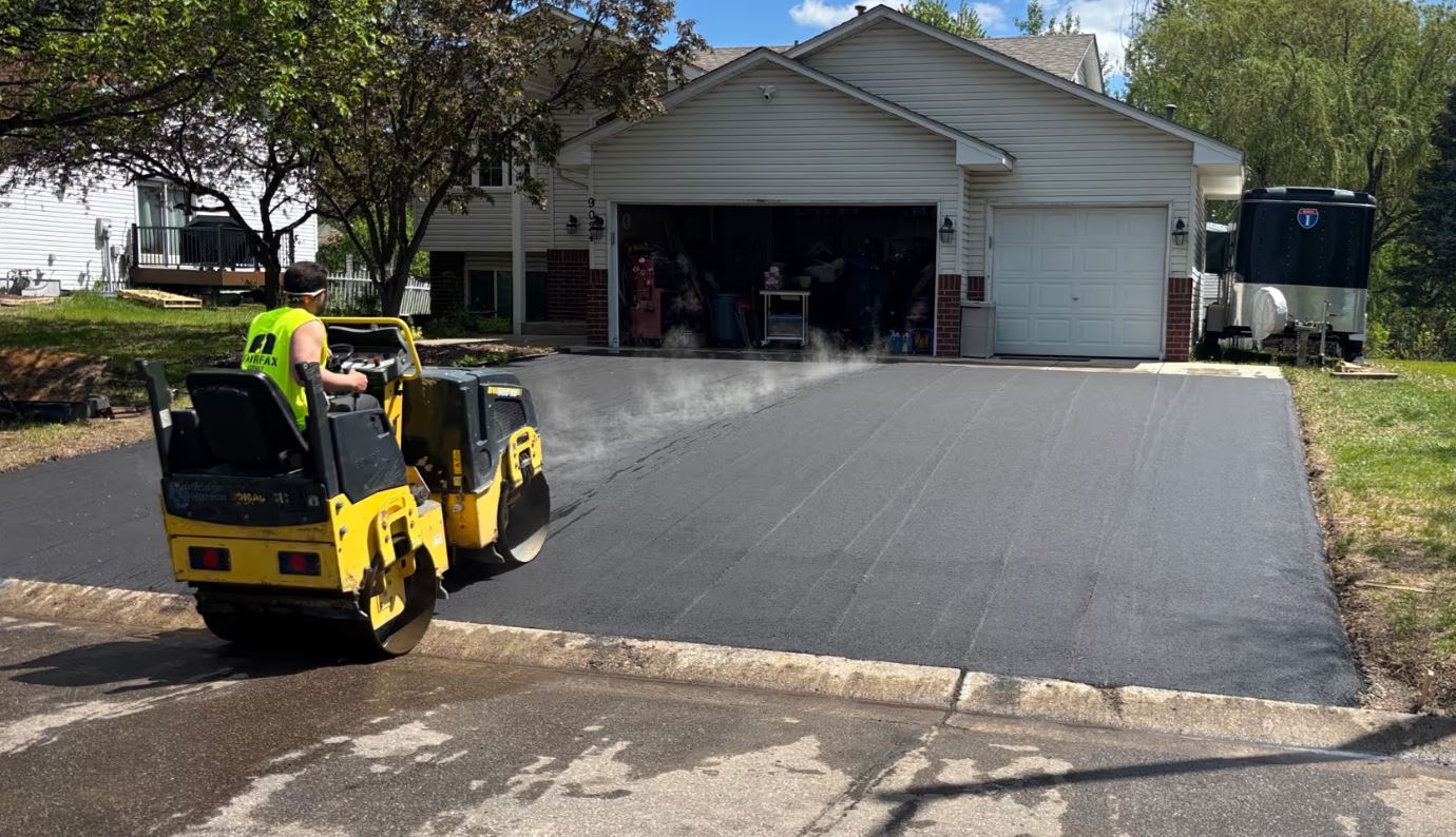 Worker compacting fresh asphalt driveway with roller